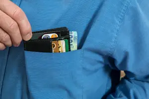 A wallet of bank cards and notes in a shirt pocket — the ordinary Jamaican starting point for a cash purchase