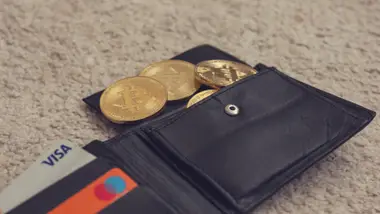 A wallet holding physical Bitcoin tokens and bank cards, the custody question at the centre of this guide